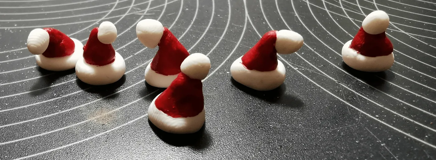 Six tiny red-and-white Santa hats, sculpted for miniatures, on a cutting mat
