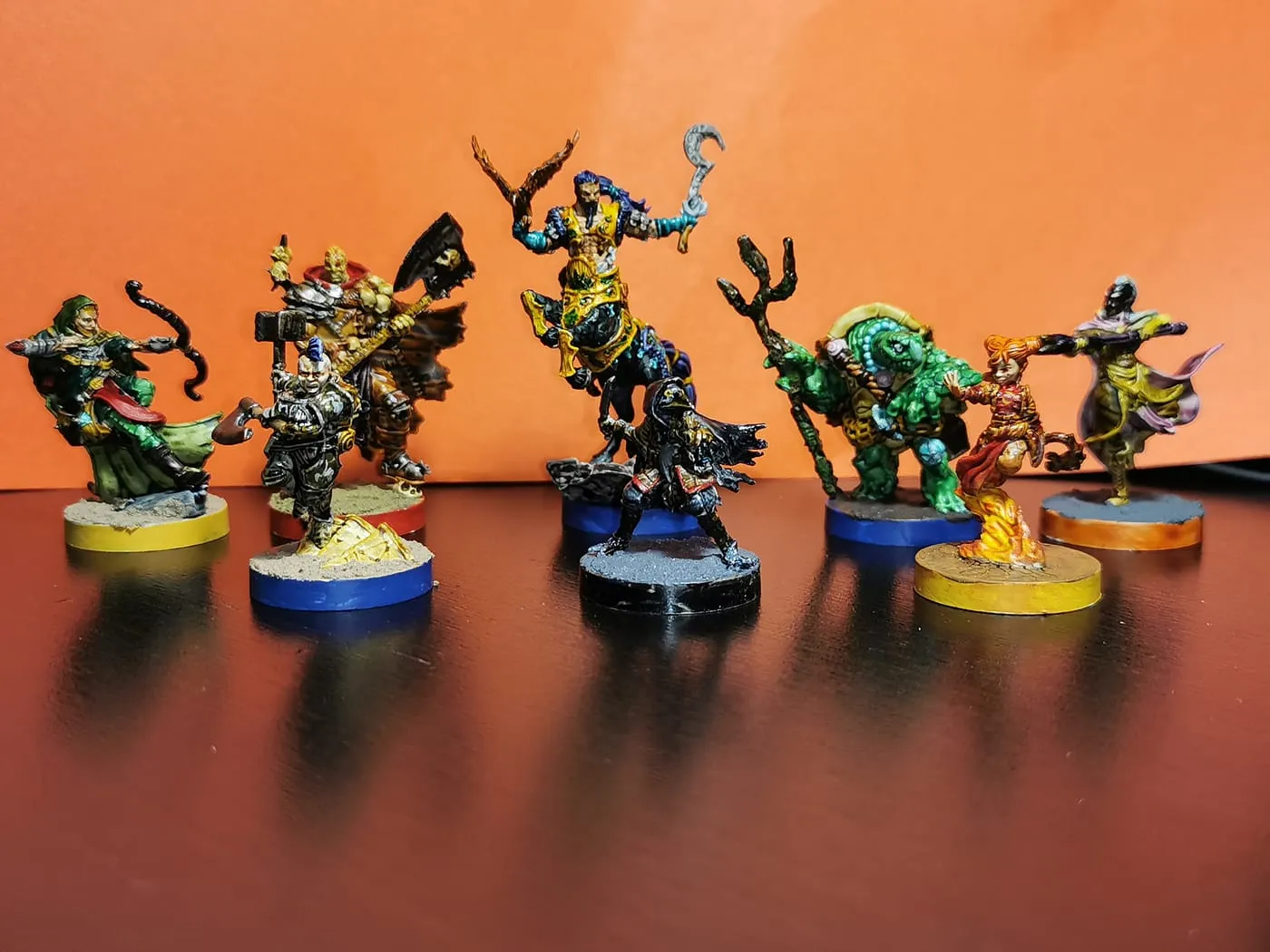 Eight painted hero miniatures on coloured bases against an orange background